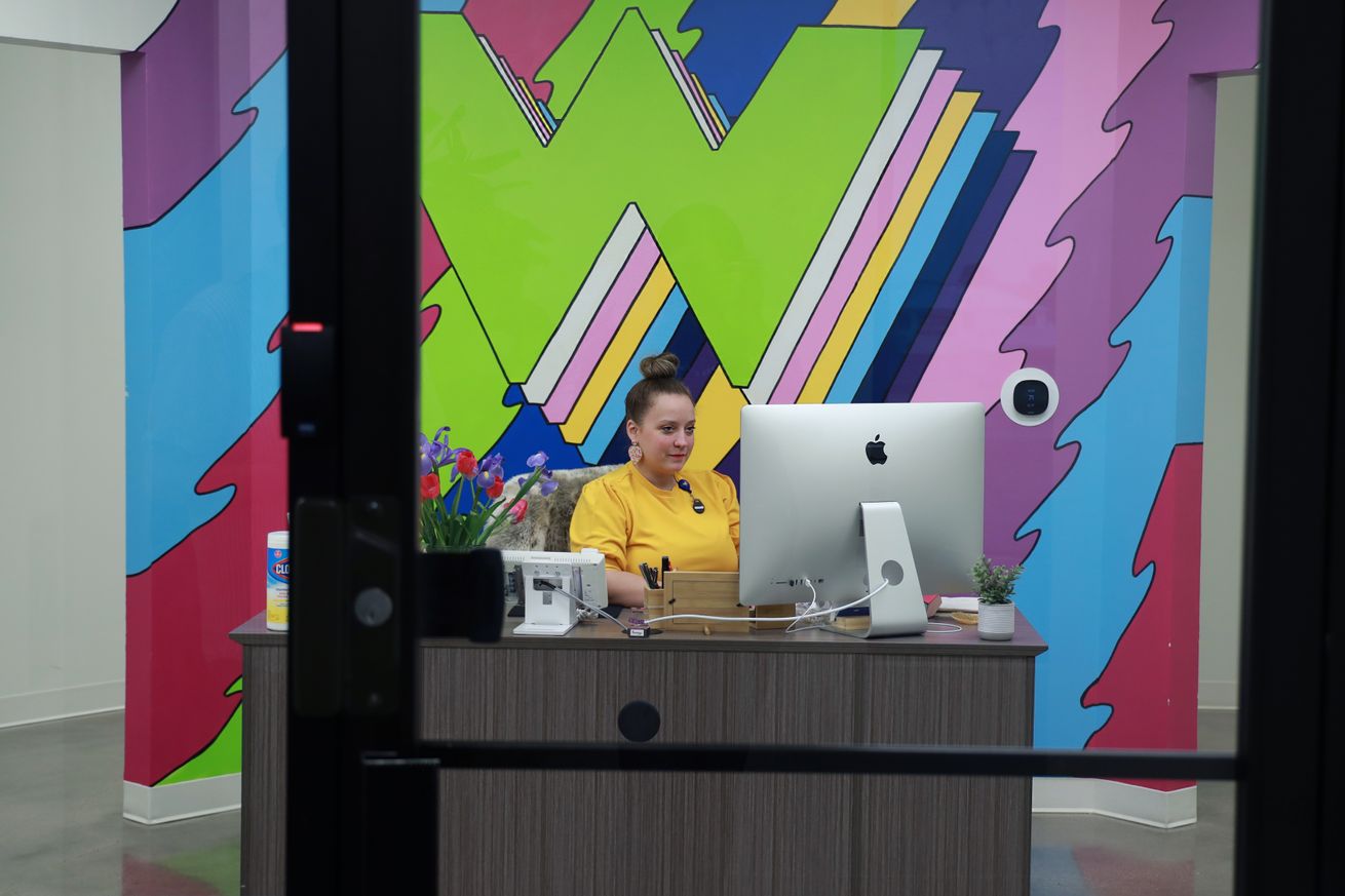 Image of Morgan manning the front desk, with a Wonder Works mural behind her.